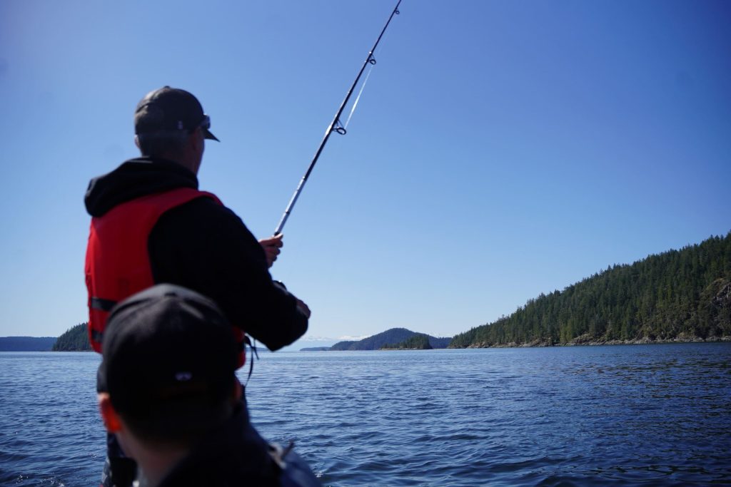 a backview of fishing off the boat with a guest watching, during a fishing charter tour from Quadra Island and Campbell River.