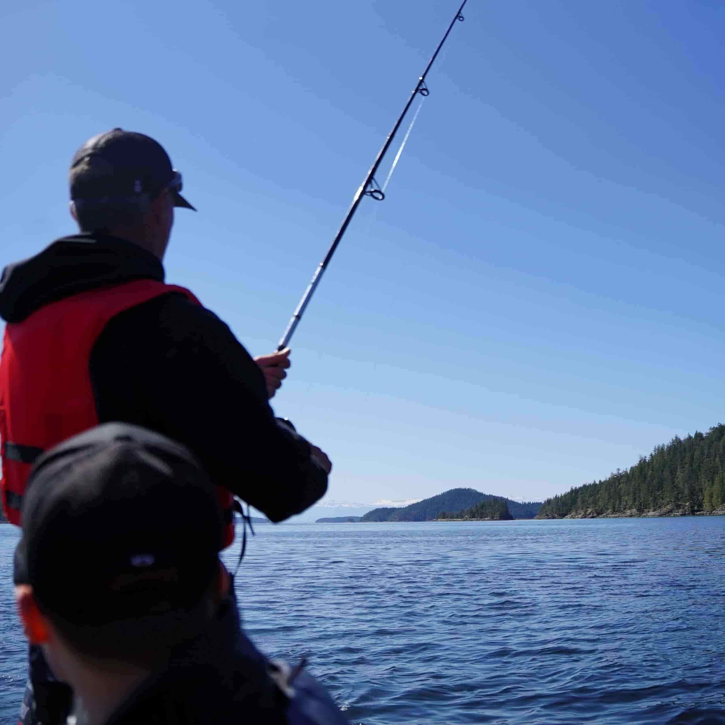 Captain Jay fishing off the side of the tour boat with a guest on a fishing charter. Coastline in the background.