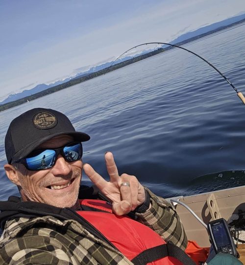 Captain taking a selfie on the ocean during a guided fishing charter tour, with the vast sea and coastline in the background.