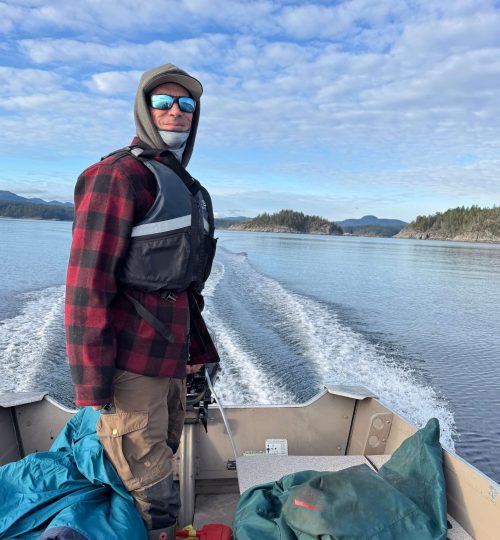 Captain smiling while standing and steering the boat on a guided fishing charter tour, with scenic coastal islands in the background.