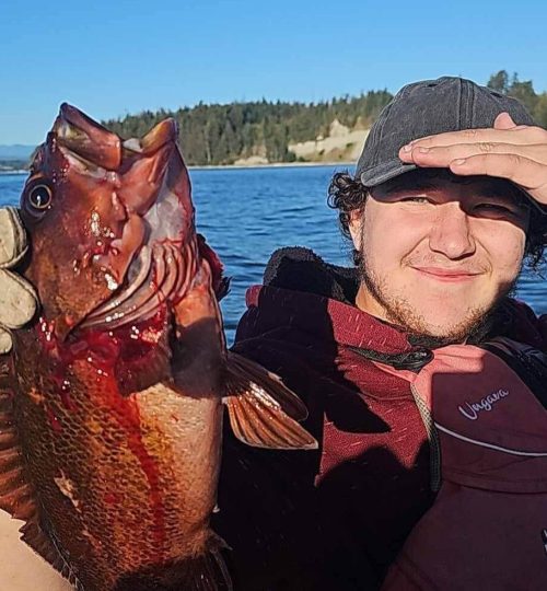 Happy visitor holding up a big fish, smiling proudly after catching it on a guided fishing charter tour. Fishing Quadra Island and campbell river